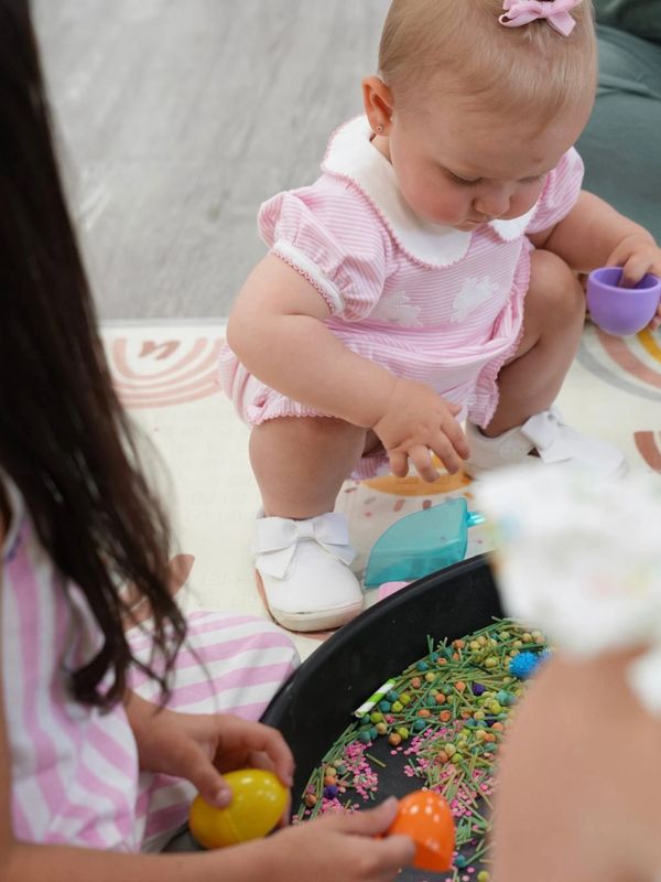 Baby in pink outfit playing with colorful toys.