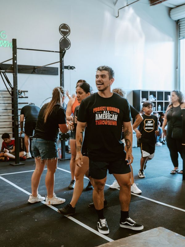 Man smiling in gym event shirt among people.