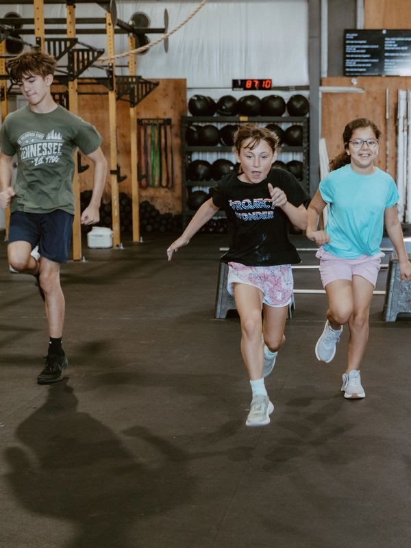 Three children running inside a gym.
