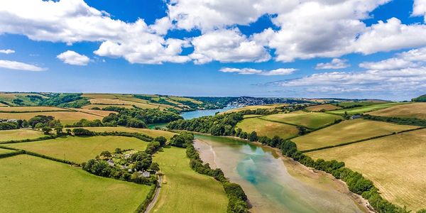 Scenic aerial view of a river winding through green fields under a partly cloudy blue sky.