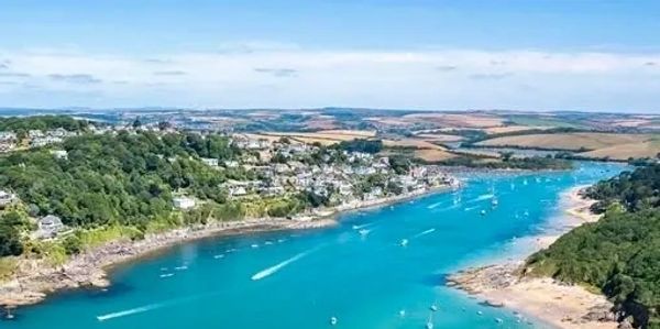 Aerial view of a blue river flowing between green hills and sandy shores with boats.