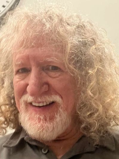 Smiling elderly man with curly white hair and beard.