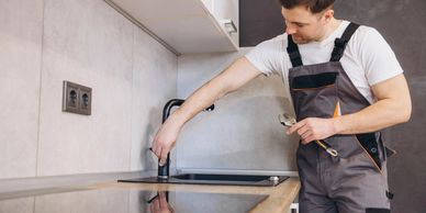 Plumber inspecting a kitchen faucet with a wrench in hand.