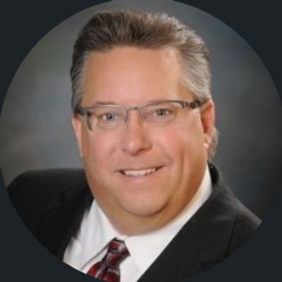 Professional headshot of a middle-aged man in glasses and suit.