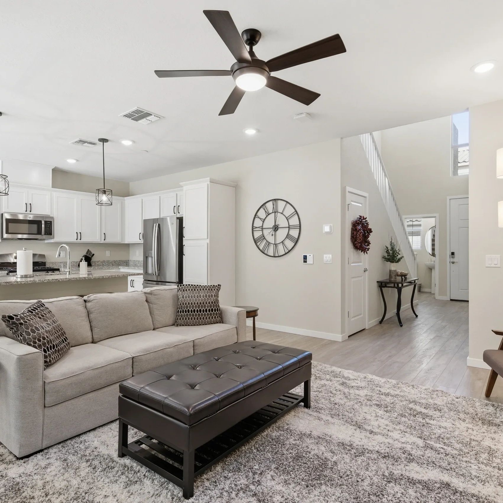 Modern living room with beige sofa, dark ottoman, and open kitchen.