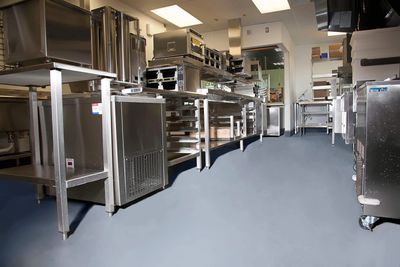 Clean, empty commercial kitchen with stainless steel appliances and workstations.