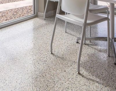 Sunlit terrazzo floor under white chairs near a glass door.