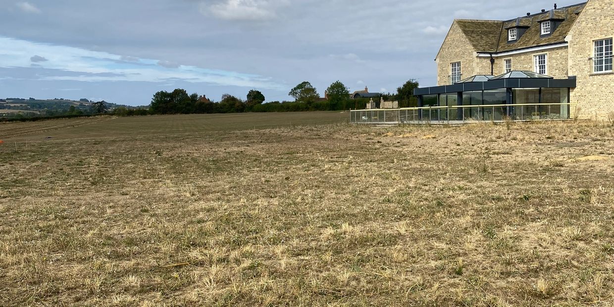 Dry grassy field beside a large stone building under a cloudy sky.