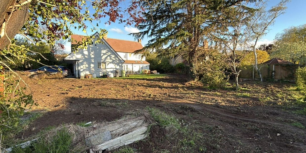View of a house with a large cleared backyard under a clear sky.