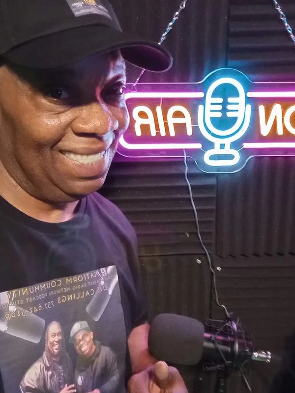 Smiling man in a podcast studio with a microphone and neon sign.