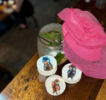 Pink hat, cocktail, and horse race-themed cookies on wooden table.