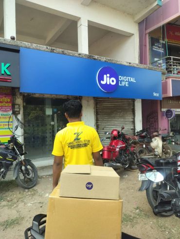 Man in yellow shirt with boxes near Jio store.