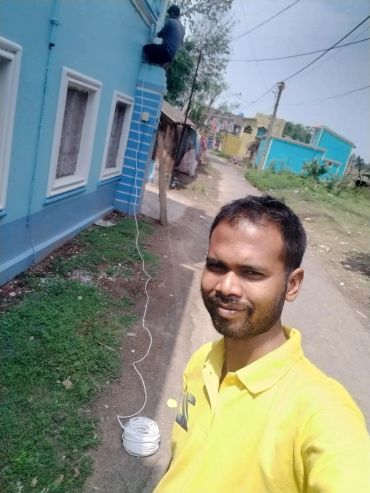 Man in yellow shirt taking selfie near blue building.