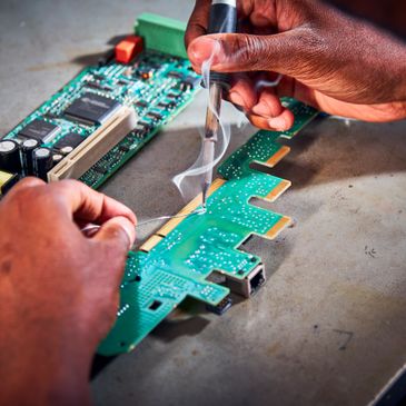 Hands soldering components on a green circuit board with a soldering iron.