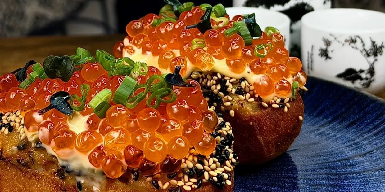 Close-up of gourmet toast topped with salmon roe, green onions, and sesame seeds.