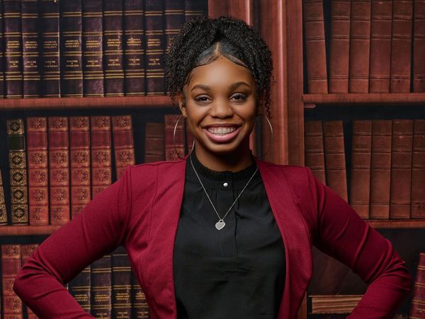 Smiling woman in a red blazer poses confidently in front of a bookshelf.