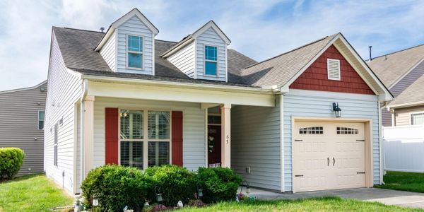 Charming suburban house with a porch and attached garage under a blue sky.