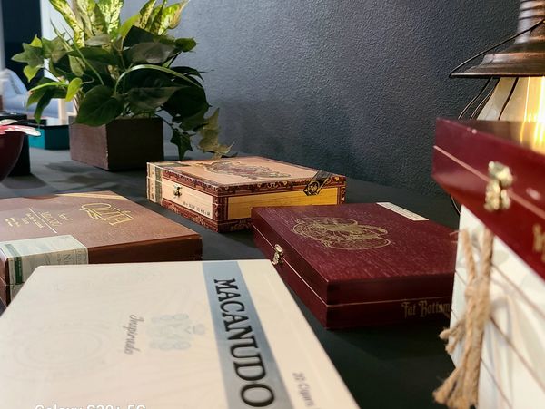 Decorative cigar boxes arranged on a table with a plant and lantern in the background.
