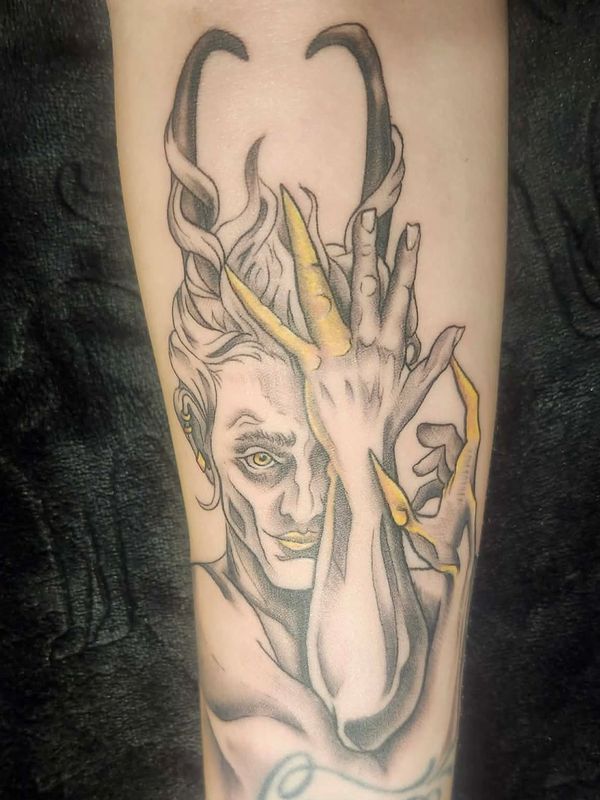 Black and gray depiction of the trickster god Loki on the forearm with gold accents 