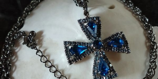 Silver chain necklace with a blue gem-studded cross pendant on a white shell.