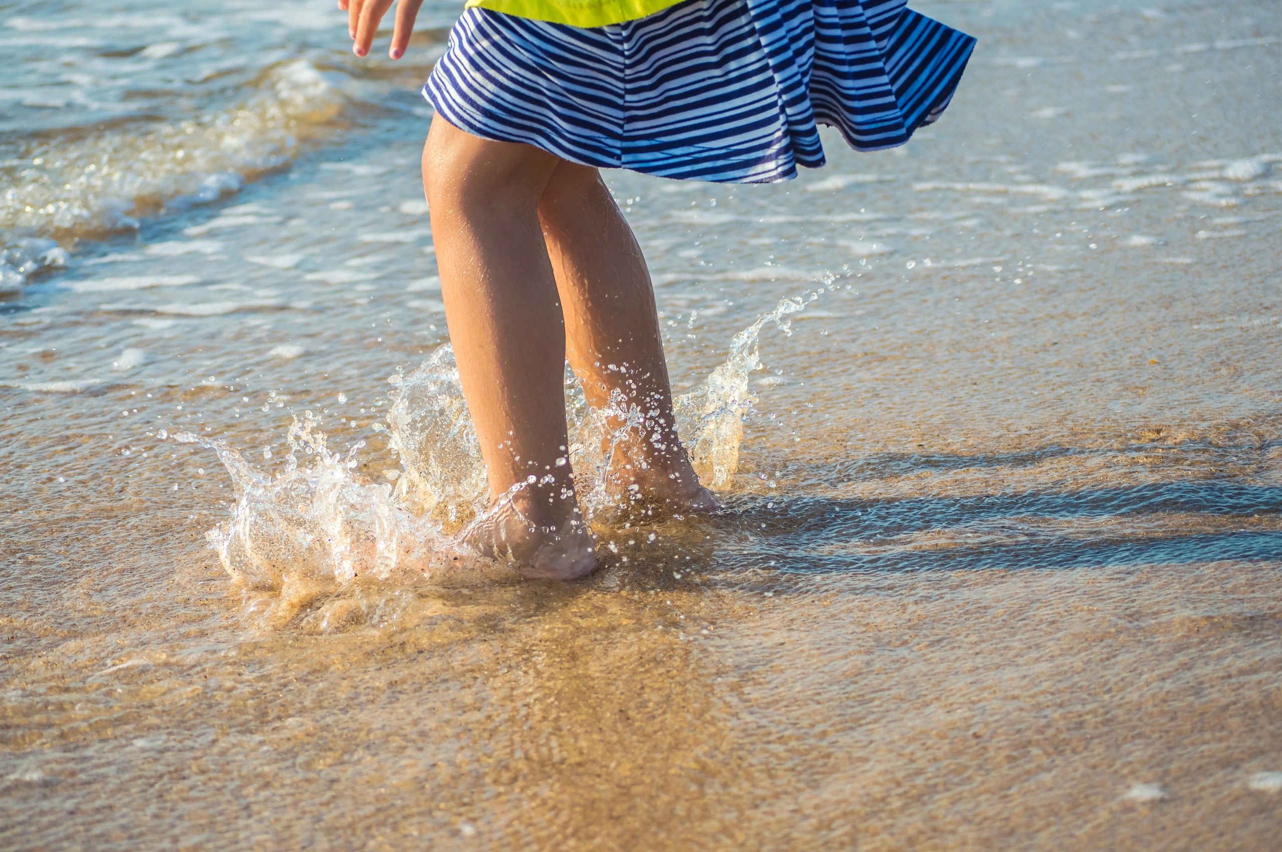 Child splashing water while wearing striped skirt