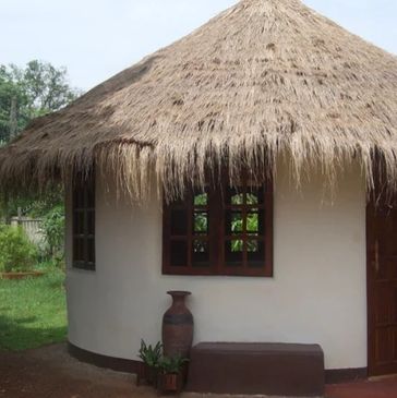Round hut with thatched roof and small window in a green setting.