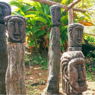 Stone statues with carved faces in a lush garden setting.