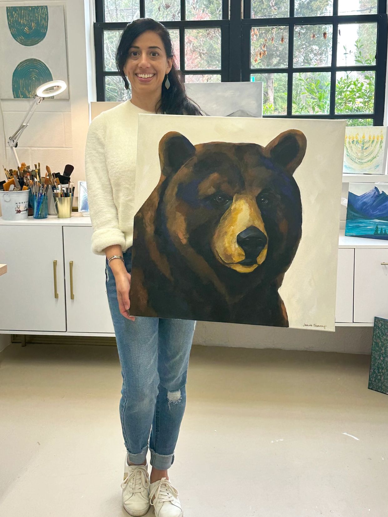 Wildlife artist Jasmine Shammay in her Atlanta based studio holding a black bear painting