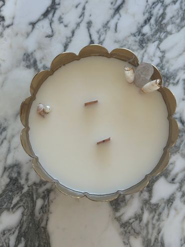 A decorative candle with two wicks and seashells in a scalloped metal container.