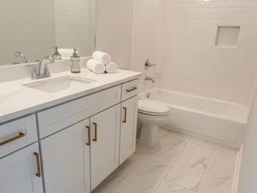 Clean, modern white bathroom with gold hardware and marble floor.