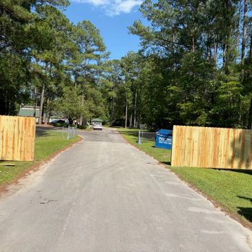 A paved road with open wooden gates and trees on both sides.