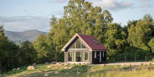 Small cabin in a green landscape with trees and mountains.