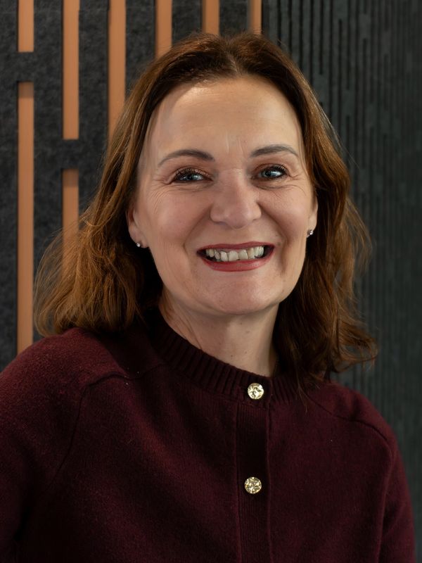 Smiling middle-aged woman in a burgundy sweater with gold buttons.