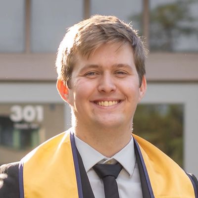 Young man smiling in graduation attire outdoors.