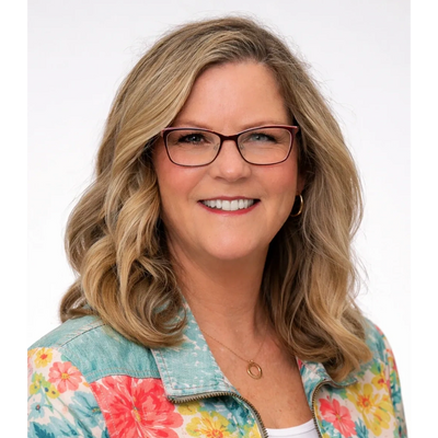 Smiling woman with glasses and wavy blonde hair in a floral jacket.