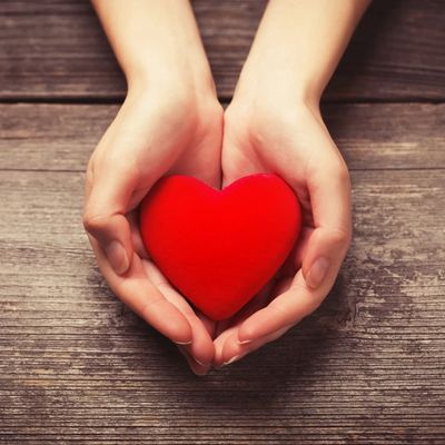 Hands gently holding a red heart on a wooden surface.