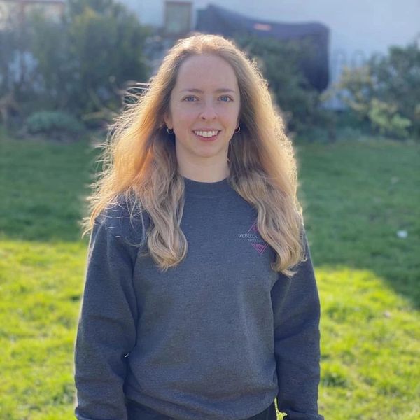 Young woman with long blonde hair smiling outdoors on a sunny day.