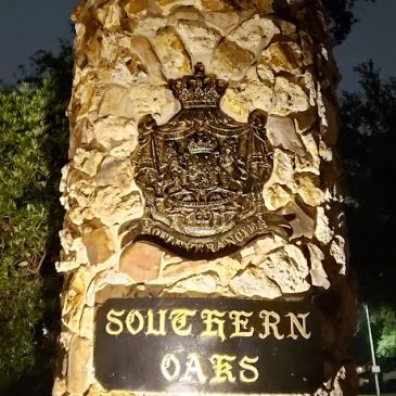 Stone pillar with Southern Oaks sign and crest at night.