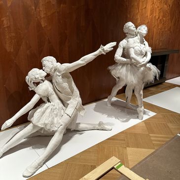 White sculptures of ballet dancers in expressive poses against a wooden wall.