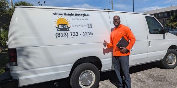 Man in orange shirt giving thumbs up next to a white van with autoglass sign.