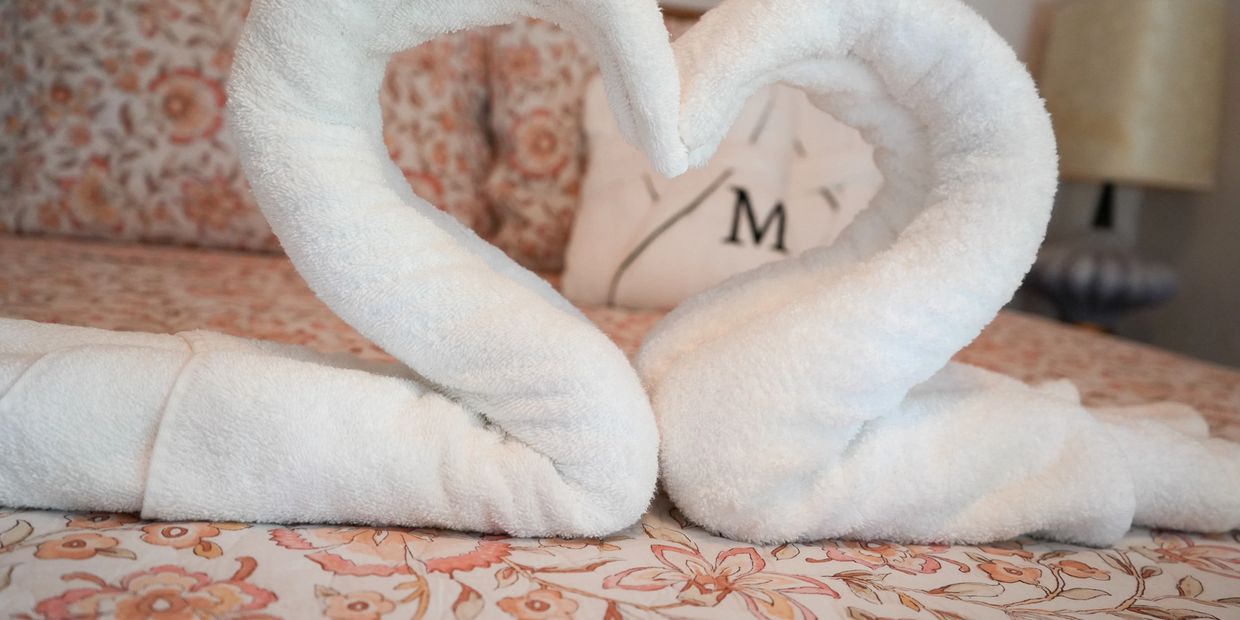 Two white towels folded into heart shapes on a floral bedspread.