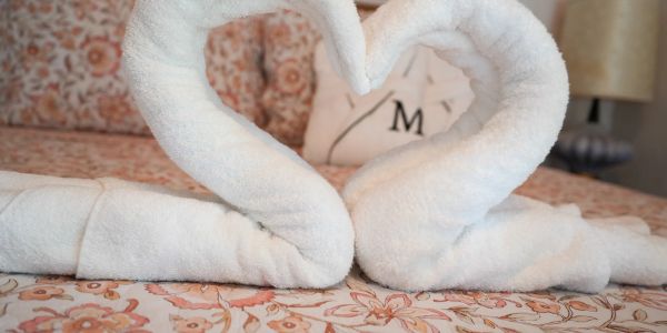Two white towels folded into heart shapes on a floral bedspread.