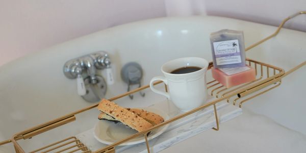 Bathtub tray holding coffee, biscotti, and soap for a relaxing bath.