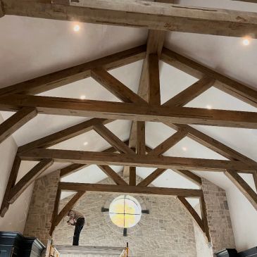 Rustic wooden beams support a high vaulted ceiling in a stone-walled room.