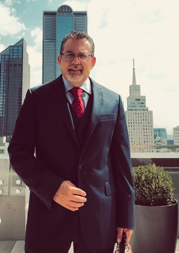 Man in suit standing on rooftop with city skyline.
