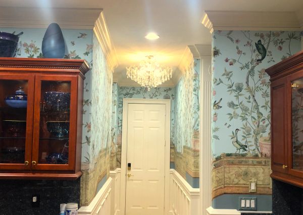 Narrow hallway with floral wallpaper and chandelier lighting.