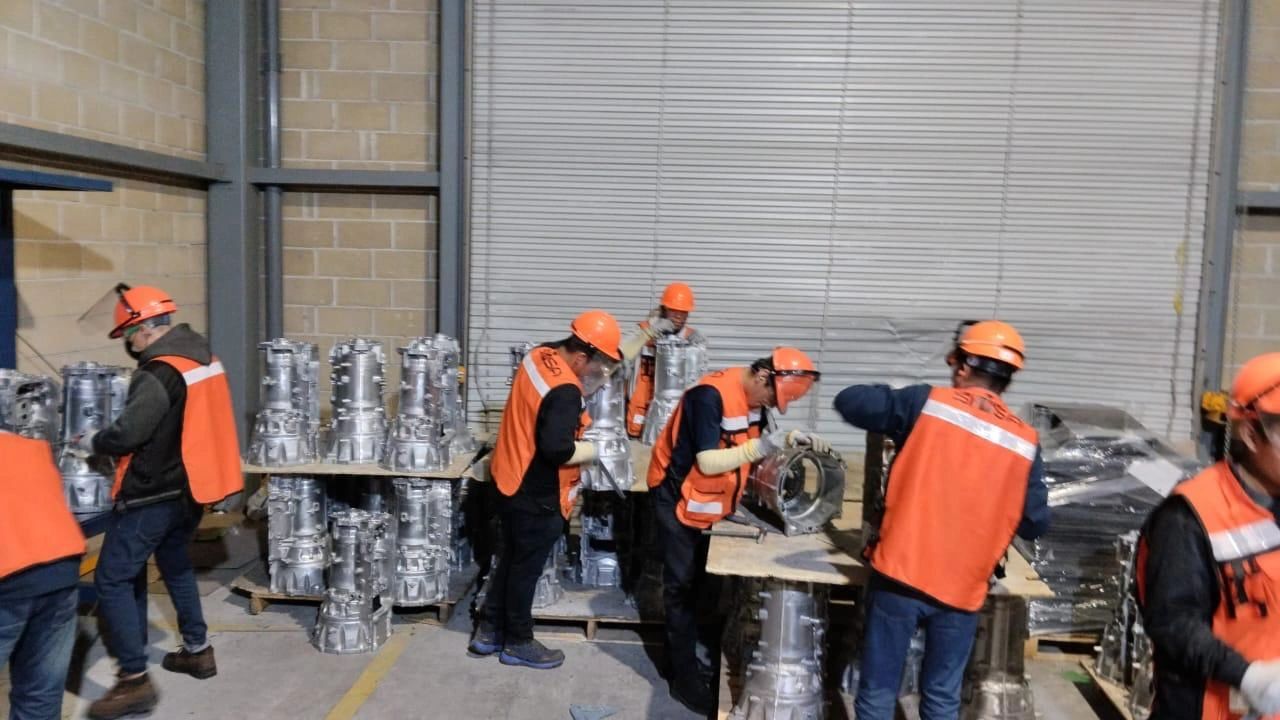 Trabajadores en fábrica inspeccionando piezas metálicas.