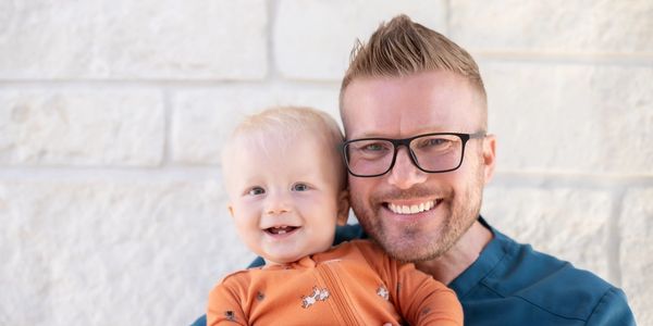 Smiling man with baby in orange outfit.
