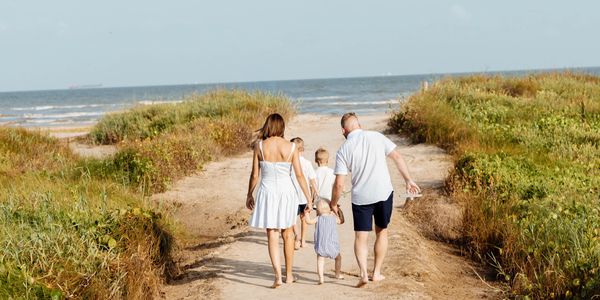 Family walking on a sandy path towards the beach.