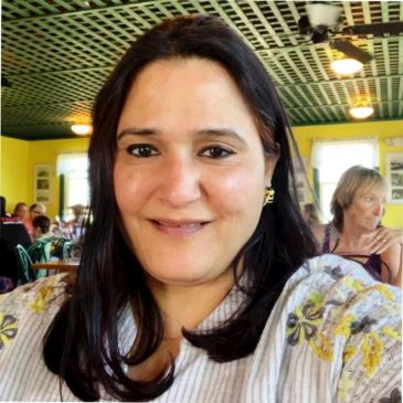 Woman smiling inside a cozy, well-lit restaurant with green ceiling and yellow walls.